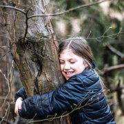 Une jeune fille souriante étreint un arbre dans un cadre forestier serein, profitant de la nature.