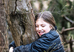 Une jeune fille souriante étreint un arbre dans un cadre forestier serein, profitant de la nature.