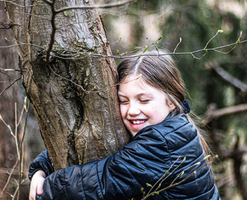 Une jeune fille souriante étreint un arbre dans un cadre forestier serein, profitant de la nature.