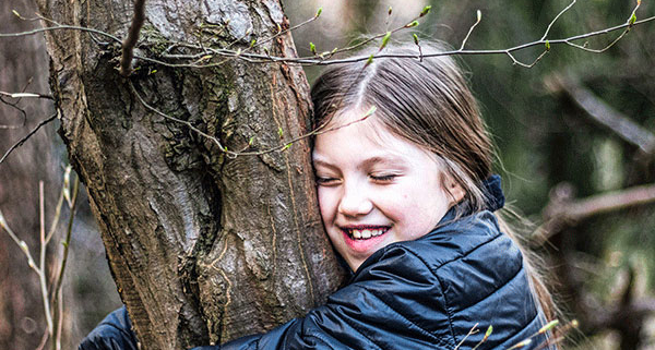 Une jeune fille souriante étreint un arbre dans un cadre forestier serein, profitant de la nature.